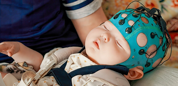 baby sleeping with blue cap and wires on it